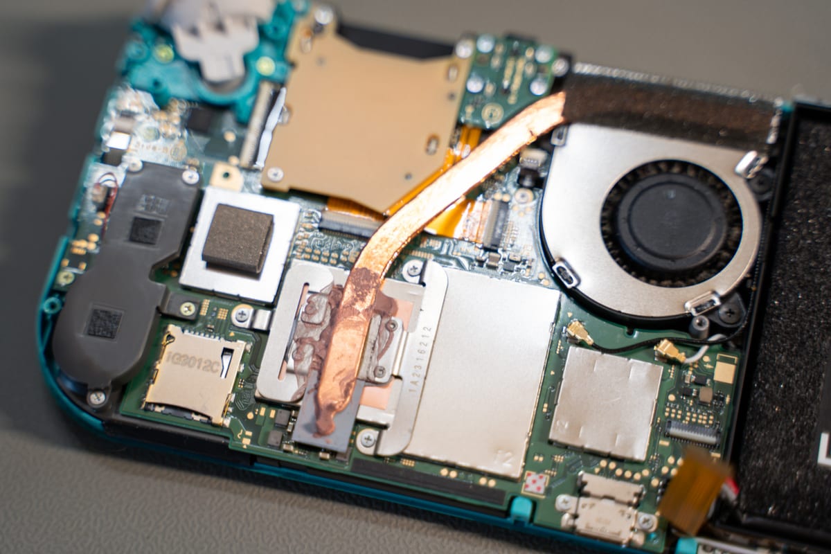 The same Switch Lite opened up on the bench, showing the cooling fan, the copper heat pipe and the old thermal paste on the processor.